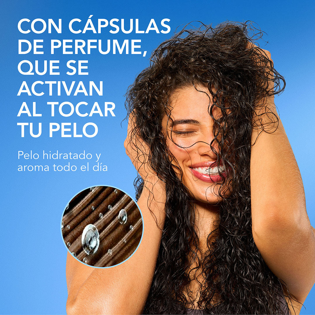 Mujer con cabello rizado tocando su cabello con detalle de cápsulas de perfume y texto Con Cápsulas de Perfume que se activan al tocar tu pelo hidratado con aroma todo el día