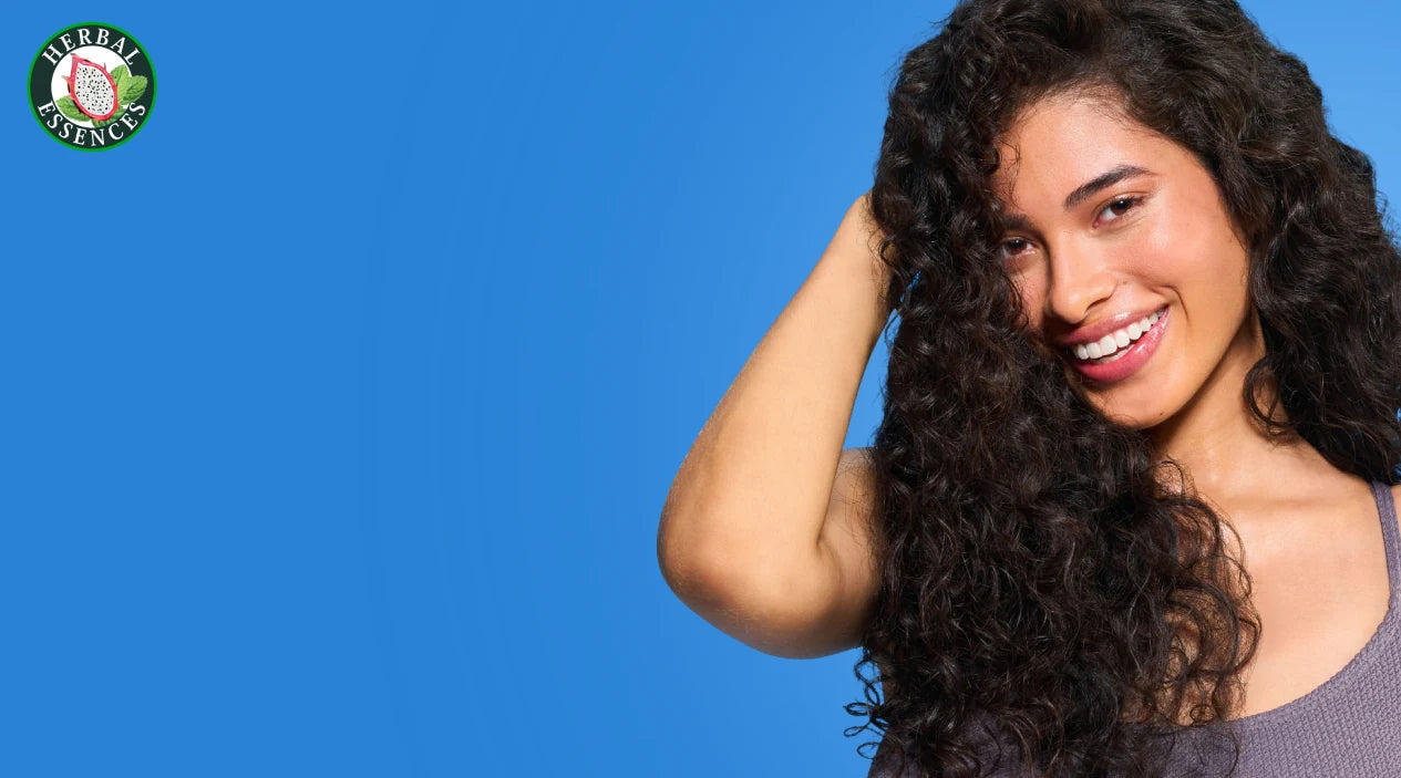 Mujer con cabello rizado sonriendo junto a Mascarilla Herbal Essences Pitahaya y Menta con texto Mascarilla Multiusos mascarilla de 3 minutos pre-shampoo y crema de peinar