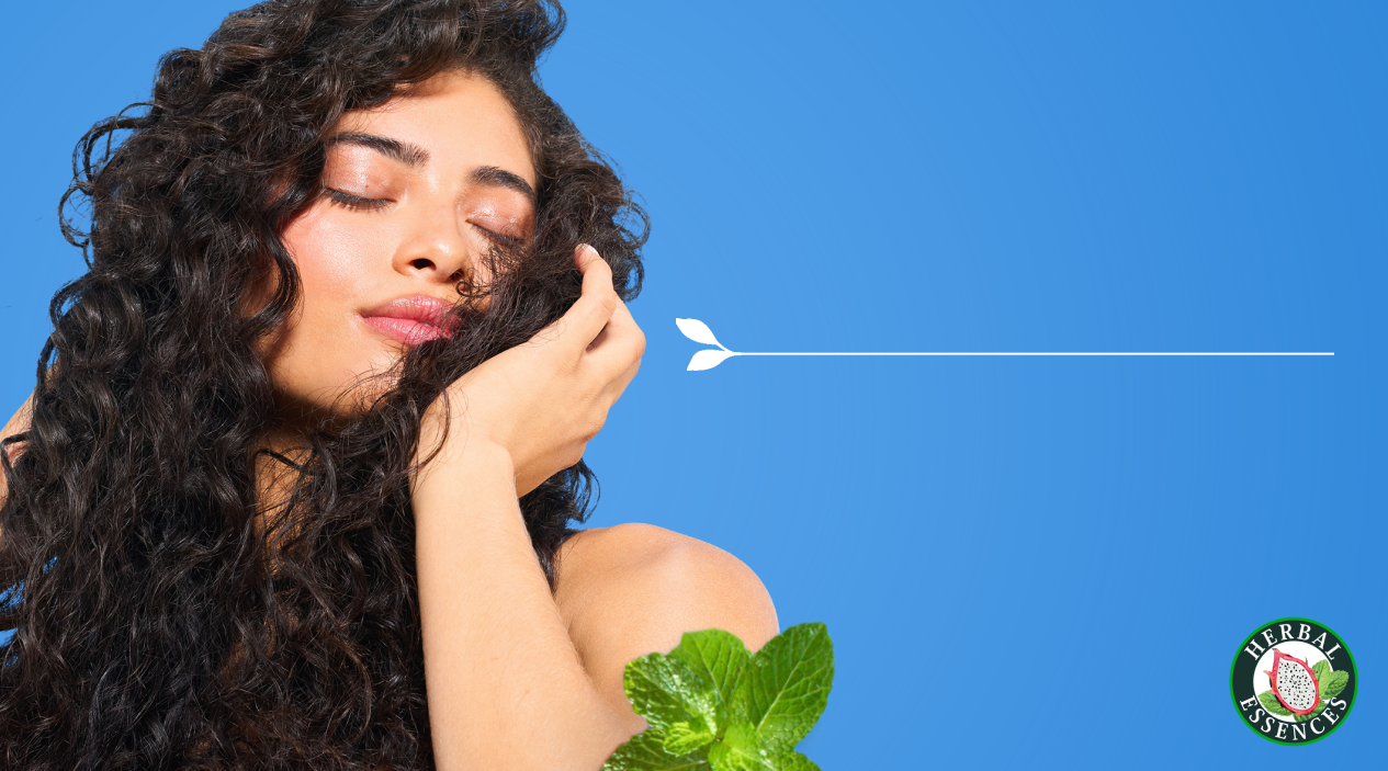 Mujer con cabello rizado tocándose el pelo con Perfume Capilar Herbal Essences y texto Controla el Frizz refresca tu look aporta brillo y suavidad