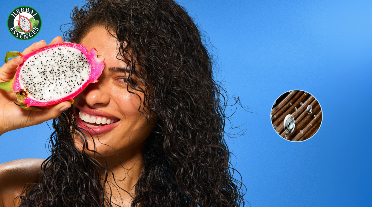 Mujer con cabello rizado sosteniendo una pitahaya cortada junto a Perfume Capilar Herbal Essences con texto Notas de Pitahaya y Sandía sinfonía de fragancias irresistibles