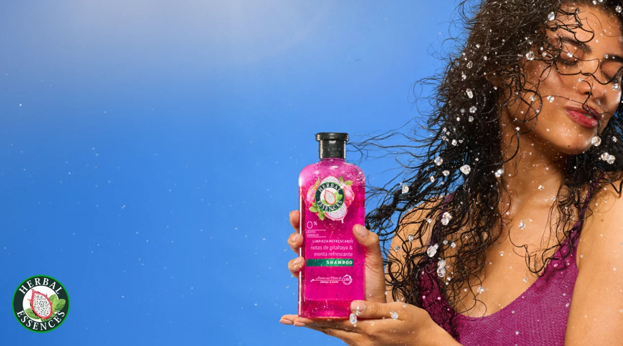 Mujer con cabello rizado sosteniendo Shampoo Herbal Essences Pitahaya y Menta con texto Limpieza Refrescante limpia oleosidad e impurezas sin resecar